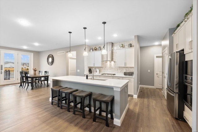 kitchen featuring wall chimney range hood, freestanding refrigerator, a sink, a kitchen breakfast bar, and tasteful backsplash