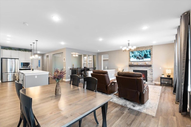 dining space with light wood-type flooring, recessed lighting, a stone fireplace, baseboards, and a chandelier