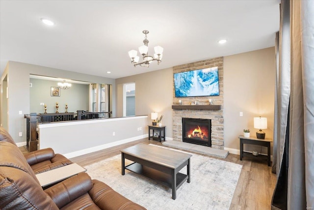 living room featuring wood finished floors, a stone fireplace, and a chandelier