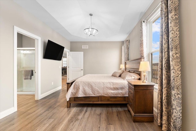 bedroom with visible vents, a raised ceiling, wood finished floors, connected bathroom, and baseboards