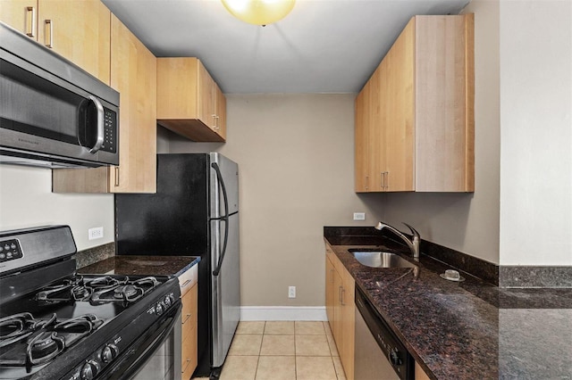 kitchen with light tile patterned floors, sink, appliances with stainless steel finishes, and dark stone countertops