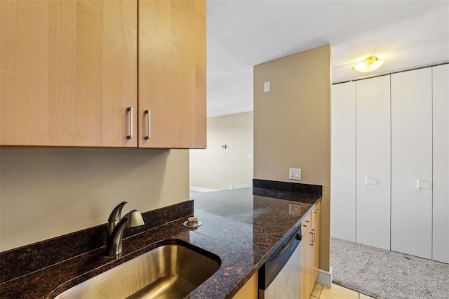 kitchen with dishwasher, dark stone counters, light brown cabinetry, sink, and light tile patterned floors