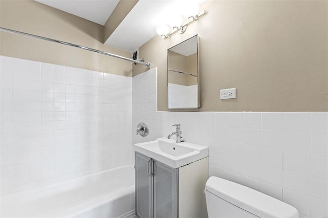 full bathroom featuring toilet, tile walls, vanity, and tiled shower / bath combo