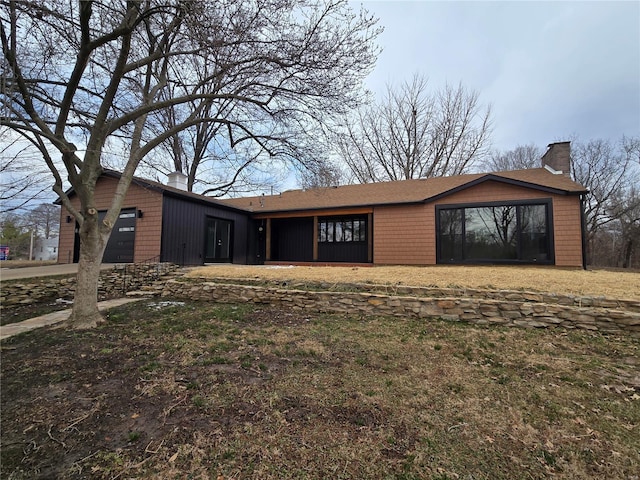 mid-century inspired home with an attached garage, a chimney, and a front lawn