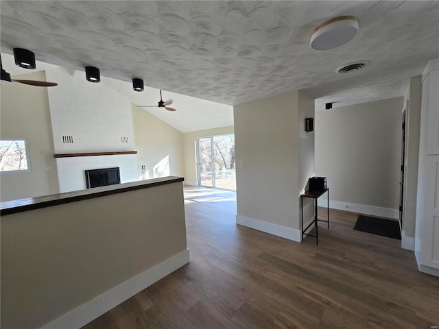 hall featuring visible vents, vaulted ceiling, a textured ceiling, wood finished floors, and baseboards