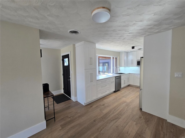 kitchen with a sink, visible vents, white cabinets, light countertops, and appliances with stainless steel finishes