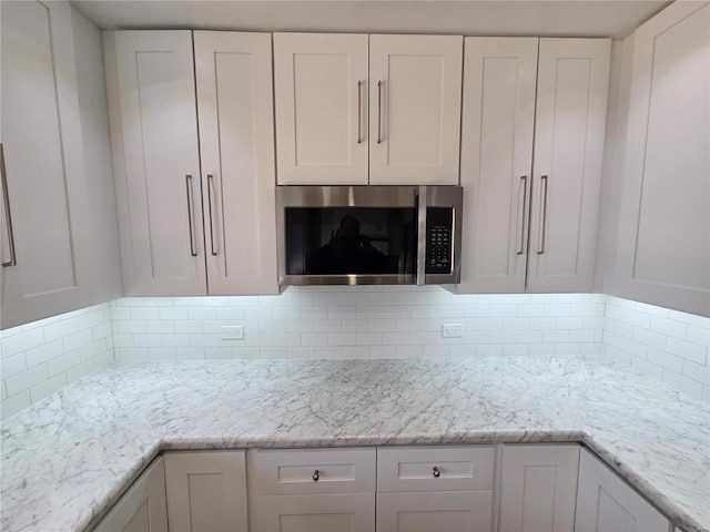 kitchen featuring white cabinets, stainless steel microwave, and decorative backsplash