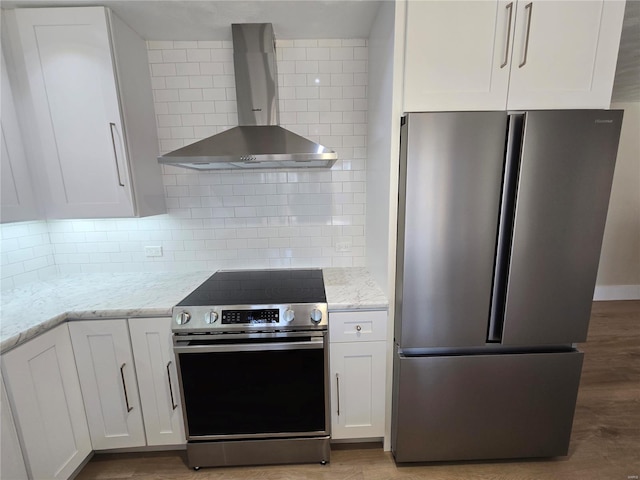 kitchen featuring stainless steel appliances, white cabinetry, wall chimney range hood, and light stone counters