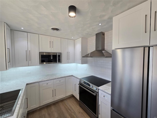 kitchen featuring visible vents, wall chimney range hood, appliances with stainless steel finishes, and white cabinets