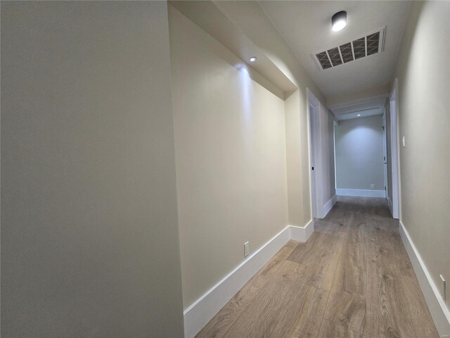 hall featuring light wood-type flooring, baseboards, and visible vents