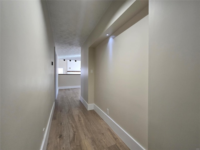 hallway with a textured ceiling, baseboards, and wood finished floors