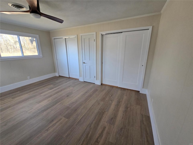 unfurnished bedroom featuring wood finished floors, visible vents, baseboards, two closets, and crown molding