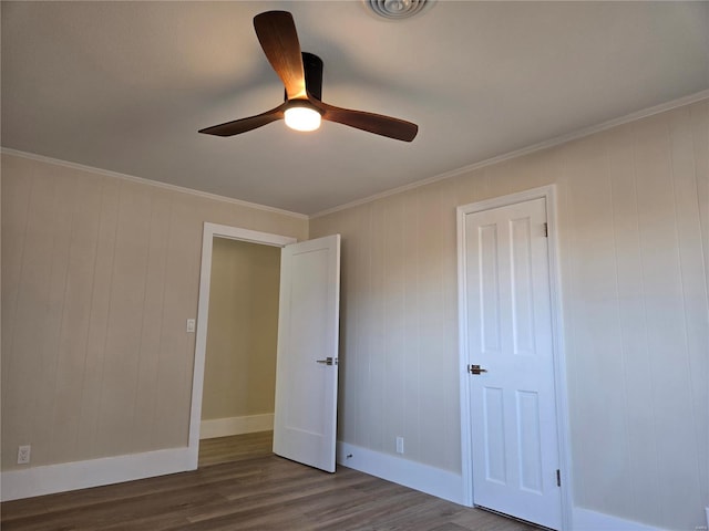 unfurnished bedroom featuring dark wood-type flooring, ornamental molding, baseboards, and ceiling fan