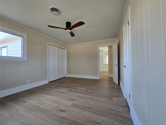 unfurnished bedroom with light wood-type flooring, multiple windows, visible vents, and crown molding