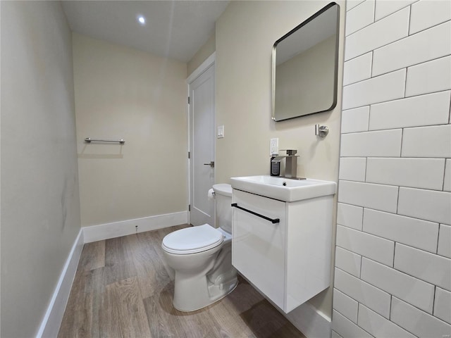 bathroom with recessed lighting, toilet, vanity, wood finished floors, and baseboards