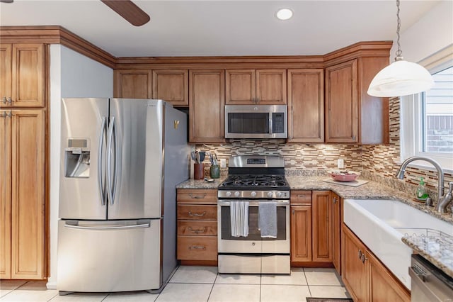 kitchen with light stone counters, hanging light fixtures, backsplash, appliances with stainless steel finishes, and sink