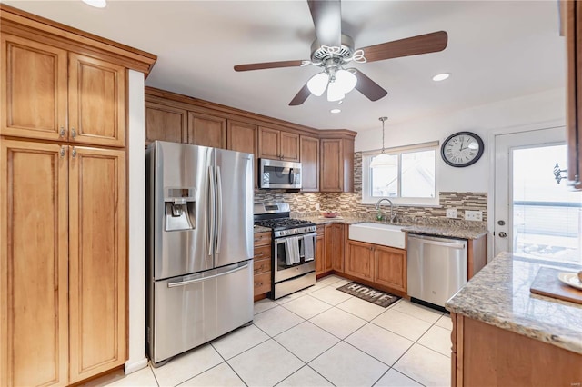 kitchen with light stone counters, decorative backsplash, appliances with stainless steel finishes, ceiling fan, and sink