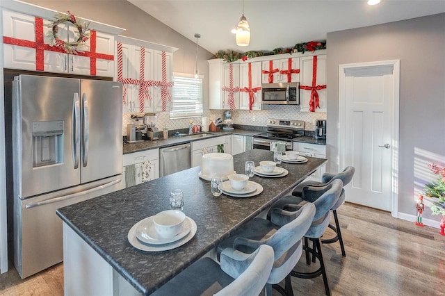 kitchen featuring a center island, backsplash, light hardwood / wood-style floors, vaulted ceiling, and appliances with stainless steel finishes