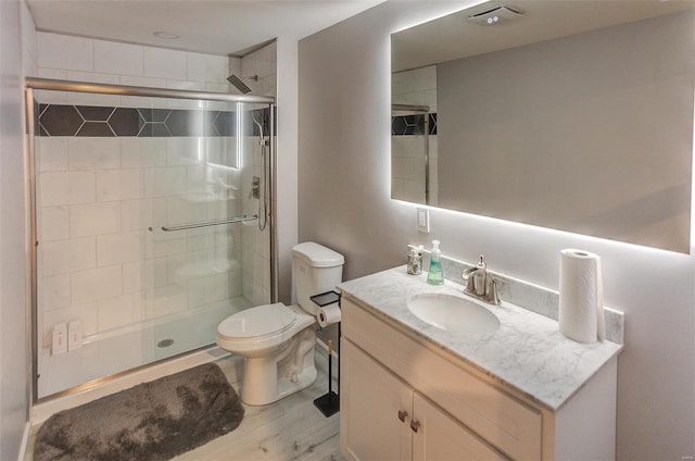 bathroom with hardwood / wood-style flooring, a shower with door, vanity, and toilet