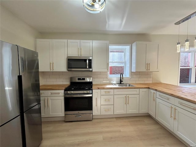 kitchen featuring pendant lighting, appliances with stainless steel finishes, wooden counters, and white cabinets