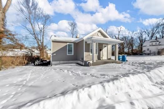 snow covered back of property featuring covered porch