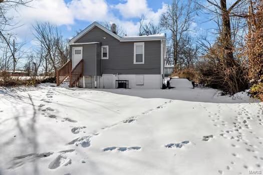 snow covered rear of property featuring central AC unit