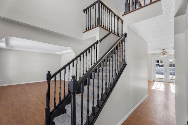 staircase featuring a textured ceiling, hardwood / wood-style flooring, french doors, a raised ceiling, and ceiling fan