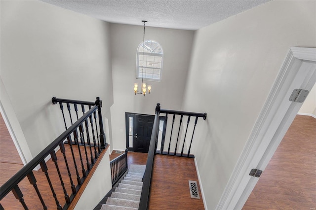 staircase with hardwood / wood-style floors, an inviting chandelier, and a textured ceiling