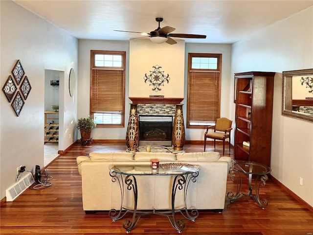 living room with dark wood-type flooring, a stone fireplace, and ceiling fan