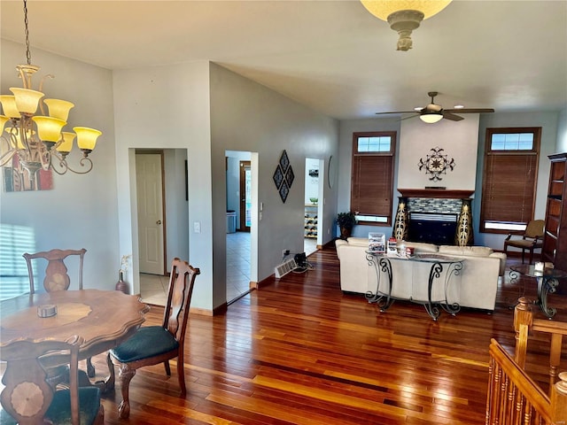 living room featuring ceiling fan with notable chandelier, a fireplace, baseboards, and hardwood / wood-style flooring