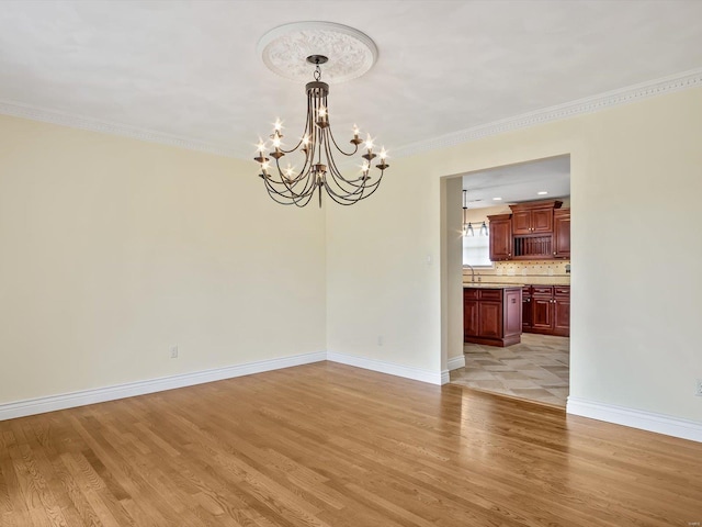 empty room with sink, light hardwood / wood-style flooring, crown molding, and a chandelier