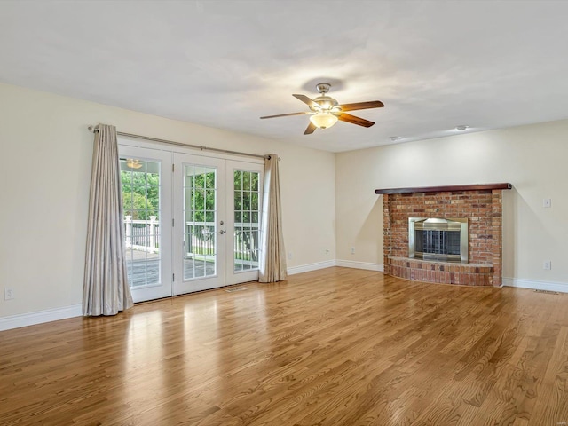 unfurnished living room featuring french doors, a brick fireplace, light wood-type flooring, and ceiling fan