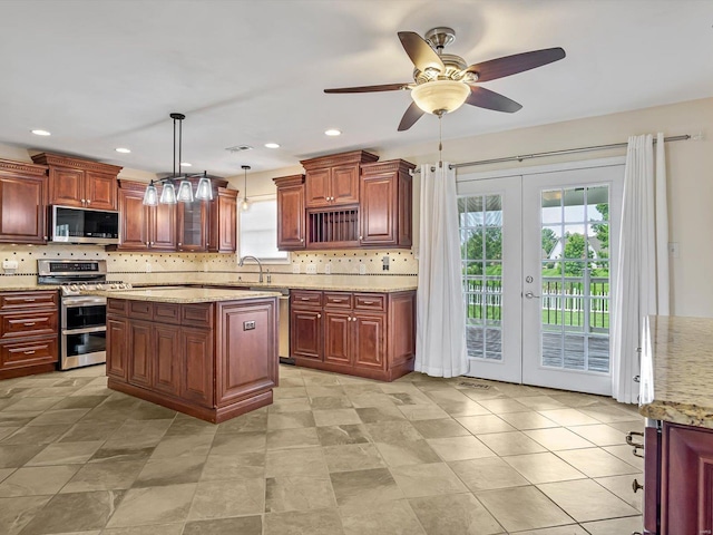 kitchen with appliances with stainless steel finishes, ceiling fan, french doors, a kitchen island, and decorative light fixtures