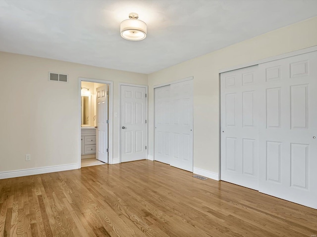 unfurnished bedroom featuring light hardwood / wood-style floors, connected bathroom, and multiple closets