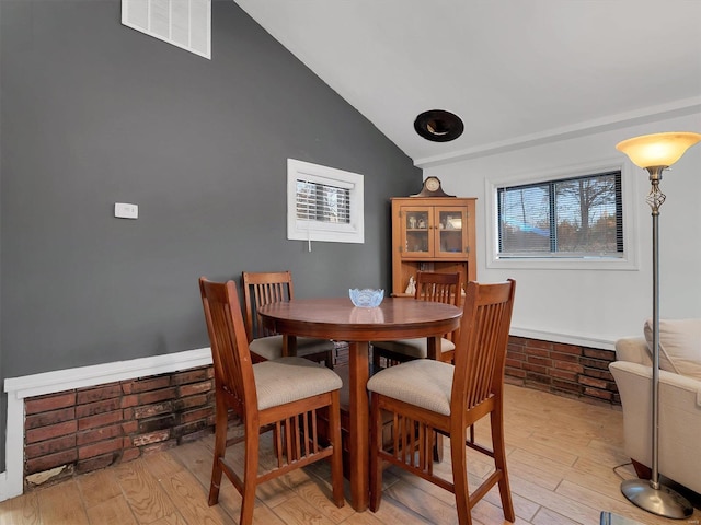 dining space with light wood finished floors, visible vents, and vaulted ceiling