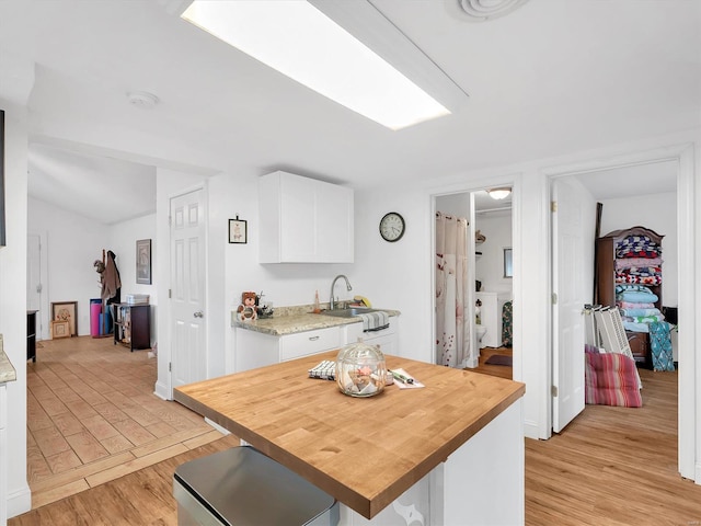 kitchen featuring a center island, wooden counters, light wood-style floors, white cabinets, and a sink