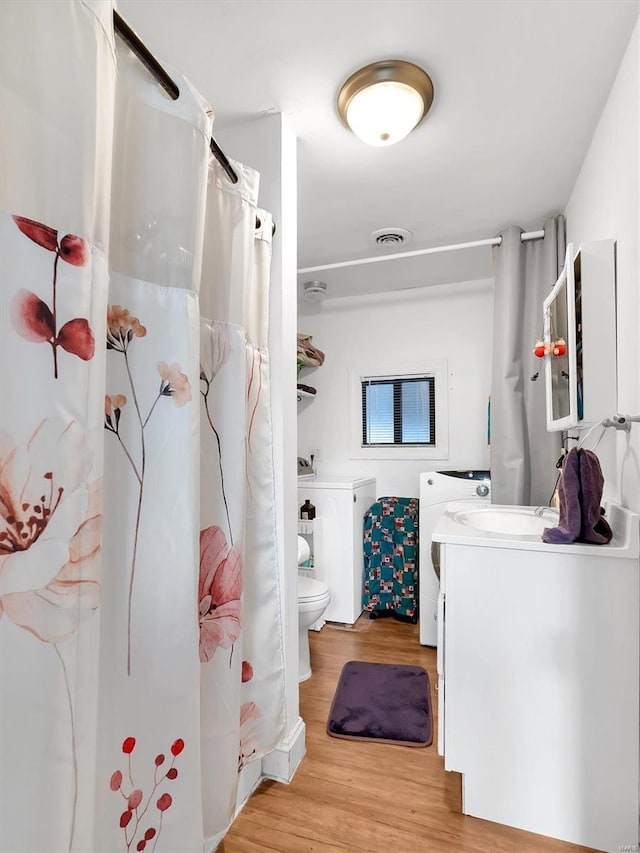 bathroom with visible vents, washer and clothes dryer, toilet, wood finished floors, and vanity