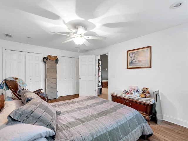 bedroom featuring ceiling fan, wood finished floors, visible vents, baseboards, and two closets