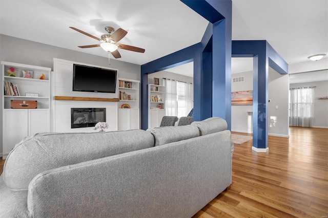 living room with ceiling fan, a fireplace, built in features, and light wood-type flooring