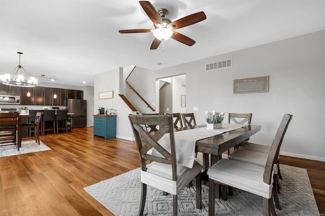 dining room featuring ceiling fan with notable chandelier and light hardwood / wood-style flooring