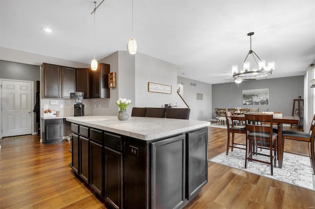 kitchen with wine cooler, dark brown cabinetry, a kitchen island, pendant lighting, and light hardwood / wood-style floors