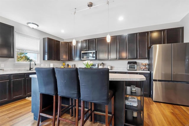 kitchen with hanging light fixtures, a kitchen bar, stainless steel appliances, light hardwood / wood-style floors, and a kitchen island