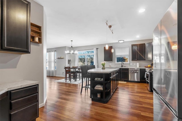 kitchen with appliances with stainless steel finishes, hanging light fixtures, dark brown cabinets, a kitchen island, and dark hardwood / wood-style flooring