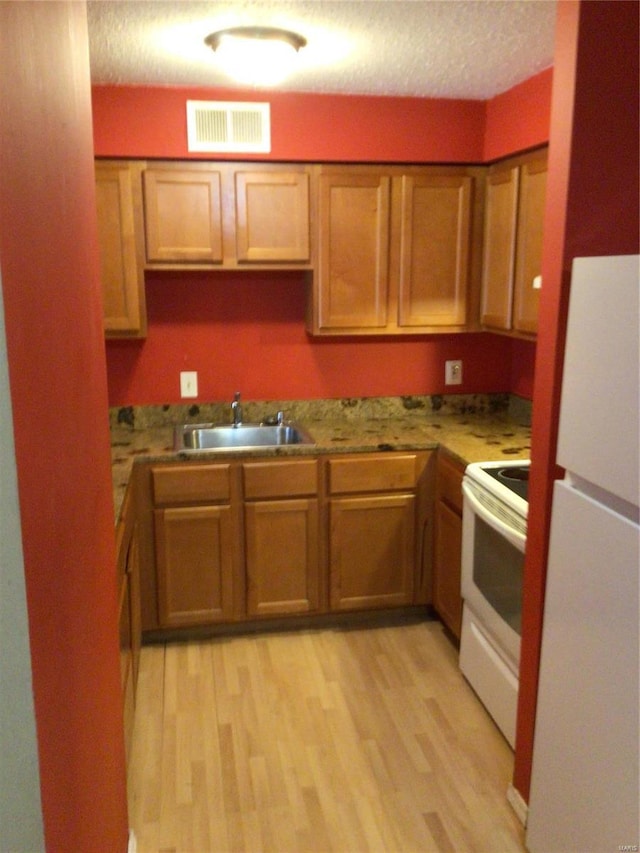 kitchen with sink, white appliances, a textured ceiling, and light wood-type flooring