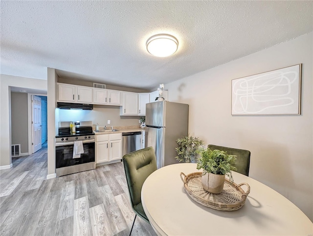 kitchen featuring appliances with stainless steel finishes, sink, white cabinets, a textured ceiling, and light hardwood / wood-style flooring