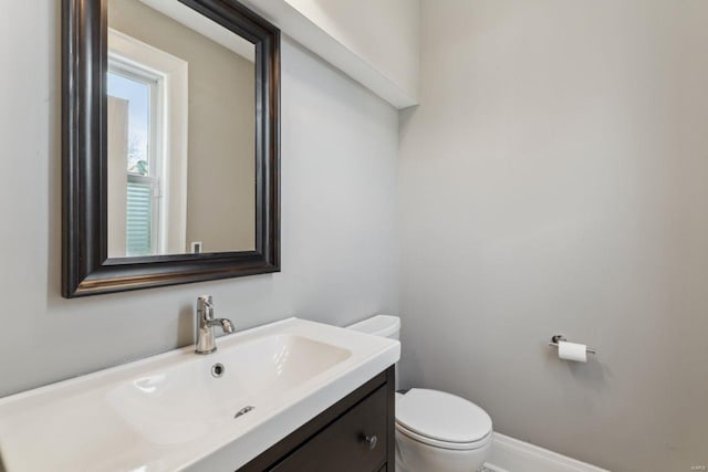 half bathroom featuring toilet, vanity, and baseboards