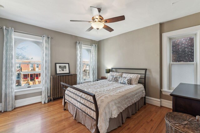 bedroom featuring light wood-style flooring, radiator, baseboards, and ceiling fan