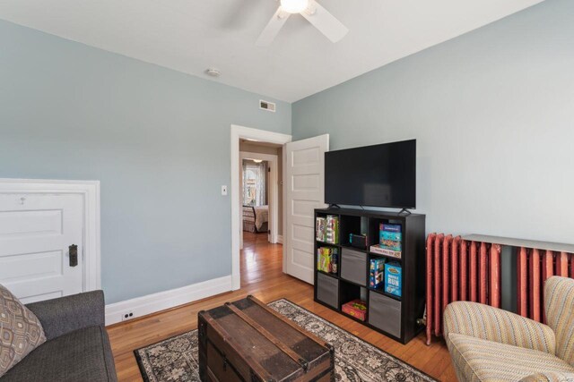 living area with visible vents, a ceiling fan, wood finished floors, radiator, and baseboards