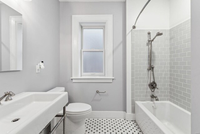 bathroom featuring tile patterned flooring, baseboards, toilet, shower / bathing tub combination, and a sink