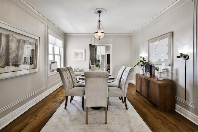 dining room featuring dark wood-style floors, crown molding, baseboards, and a decorative wall